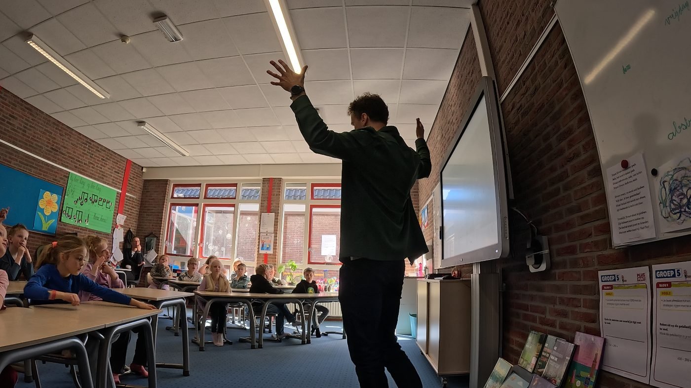 Ruben voor de klas, energiek pratend met de handen omhoog